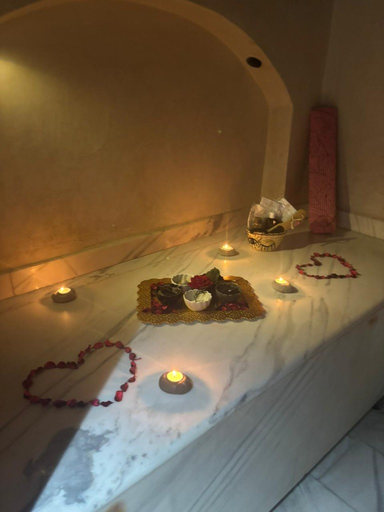 Table de soin en marbre sous une arche, bougies, pétales de rose et bols de soins.