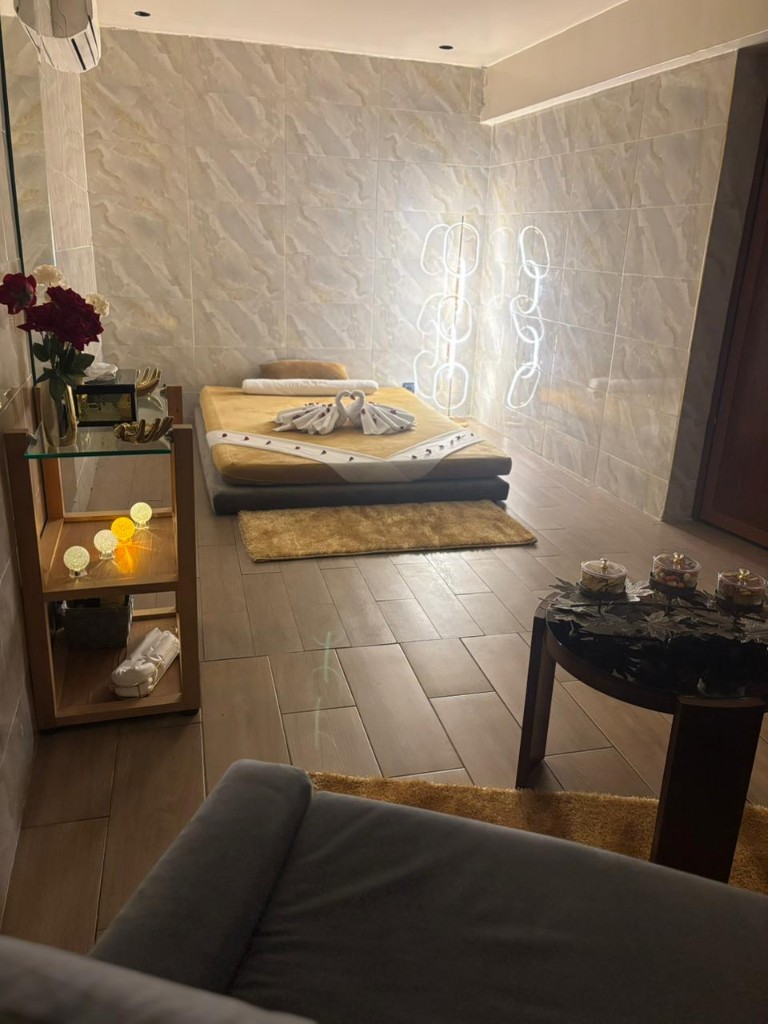 Salle de soins avec lit de massage, éclairage d'ambiance, étagères et murs en marbre.