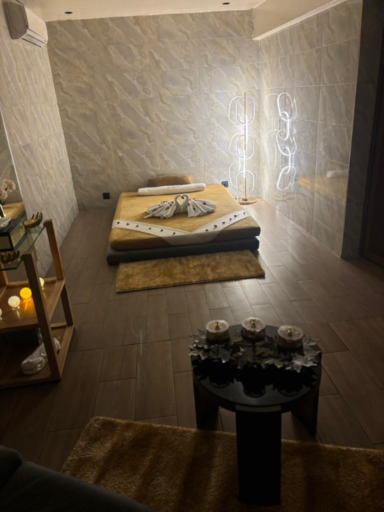 Salle de massage avec lit décoré, lampadaire moderne et lumière chaude.